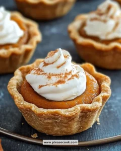 Mini pumpkin pies garnished with whipped cream on a rustic table.