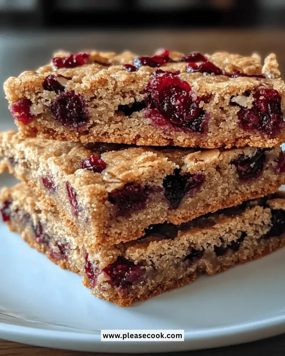 Chewy cranberry almond cookie bars on a wooden table with cranberries and almonds.
