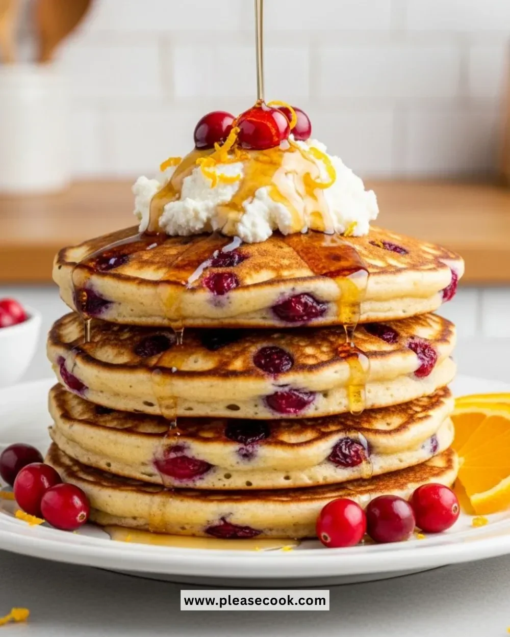 Plate of cranberry orange ricotta pancakes topped with fresh cranberries and syrup