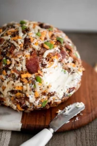 Bacon cheddar cheese ball garnished with herbs, served on a platter.
