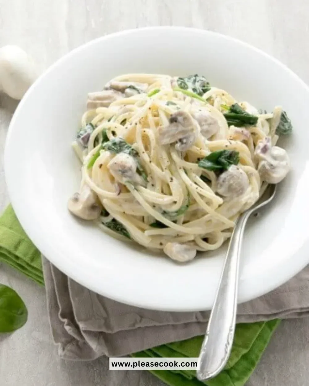 Plate of creamy mushroom and spinach spaghetti garnished with herbs