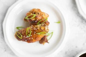 Plate of crispy baked Asian chicken wings garnished with sesame seeds and green onions