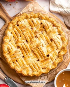 Homemade caramel apple pie topped with drizzled caramel sauce on a wooden table
