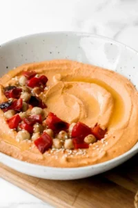 Bowl of roasted red pepper hummus with colorful vegetable sticks