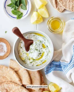 A bowl of tzatziki sauce made with yogurt, cucumber, and garlic, garnished with herbs.
