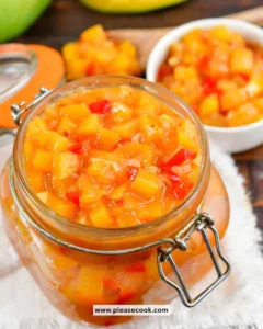 Homemade mango chutney in a jar with fresh mangoes and spices nearby.