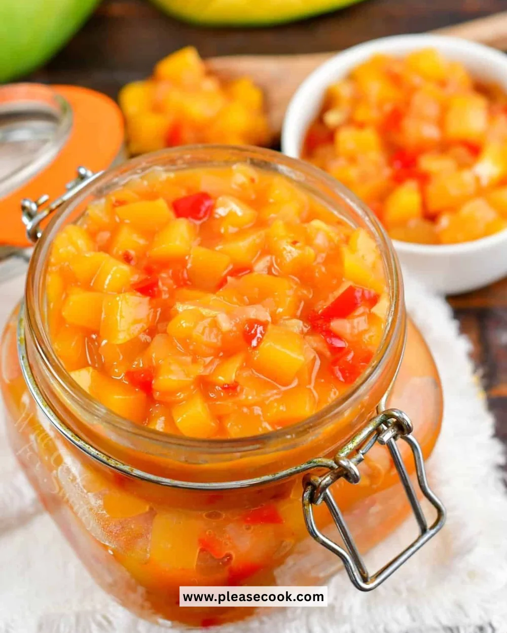 Homemade mango chutney in a jar with fresh mangoes and spices nearby.