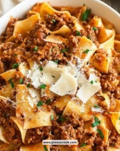 Plate of savory beef bolognese served over pasta with fresh herbs.