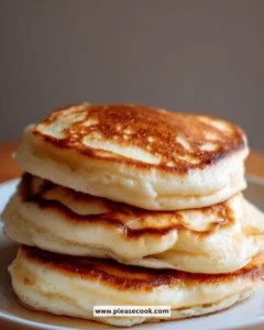 Fluffy and golden sourdough pancakes stacked on a plate with syrup and fruits