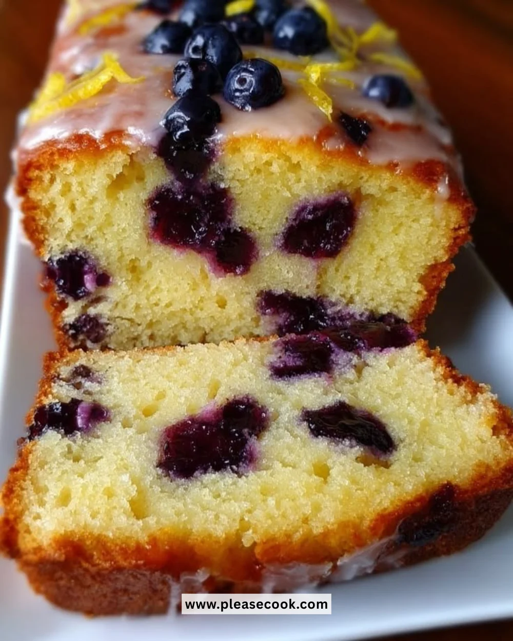 Sliced zesty lemon blueberry bread on a wooden table with fresh blueberries and lemon slices.