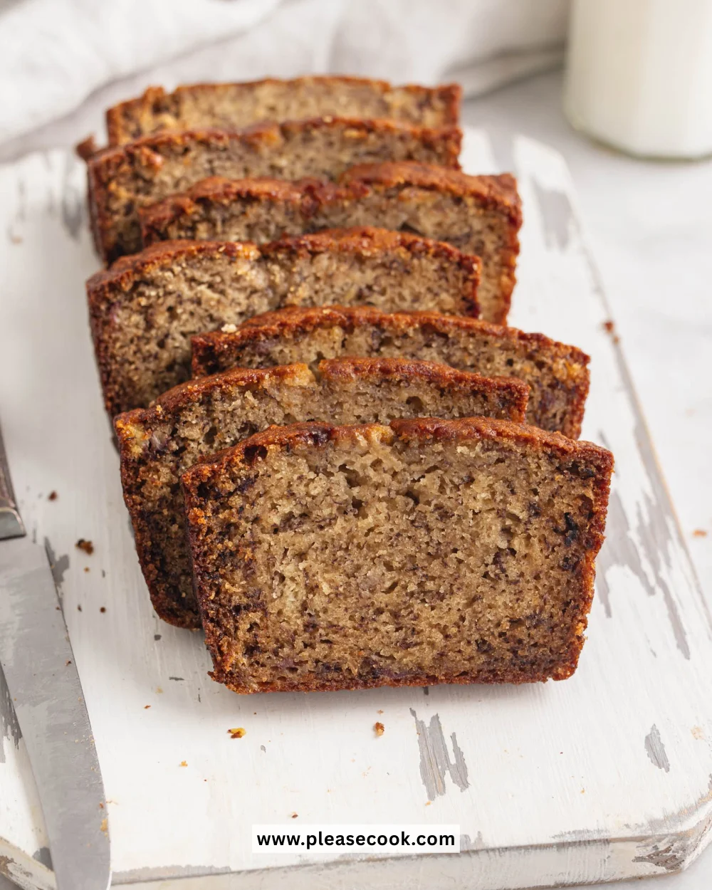 Slice of moist banana bread on a wooden table, garnished with banana slices