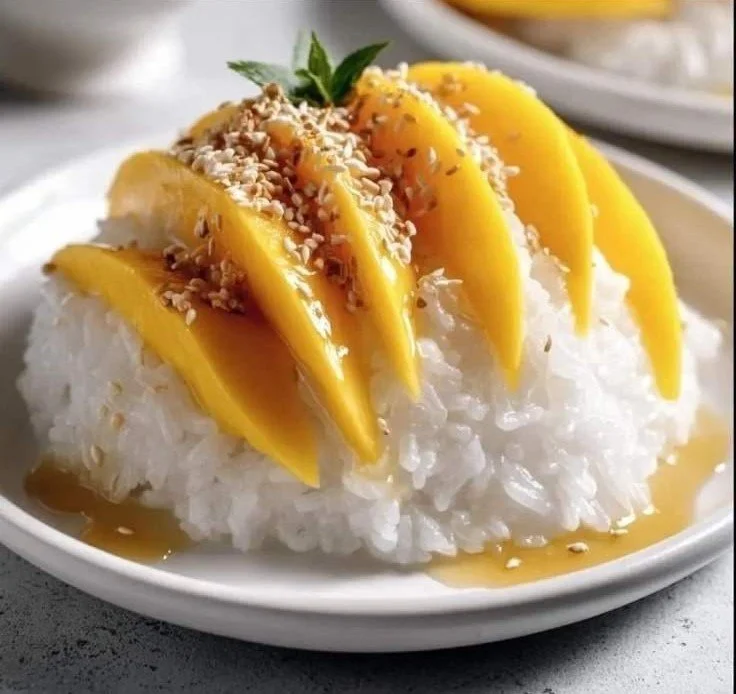 Plate of authentic mango sticky rice topped with ripe mango slices and coconut sauce.