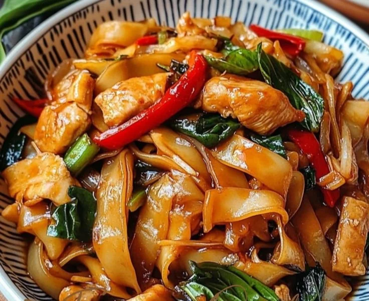 Plate of spicy drunken noodles garnished with basil and vegetables