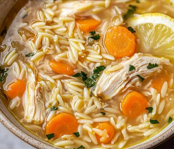 A bowl of homemade lemon chicken soup garnished with herbs.