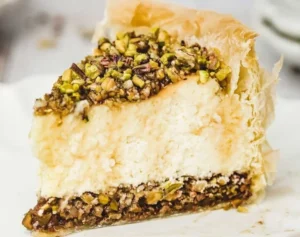 A slice of Baklava Cheesecake topped with nuts and honey.