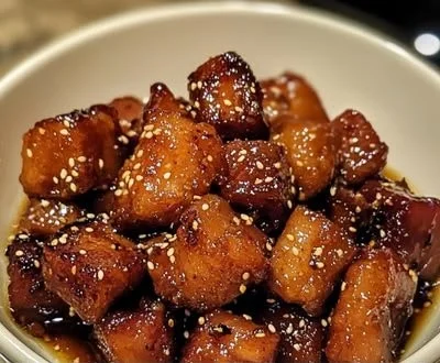 Honey garlic crispy pork belly bites on a plate garnished with herbs
