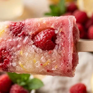 Raspberry Lemonade Protein Popsicles on a wooden table with fresh raspberries